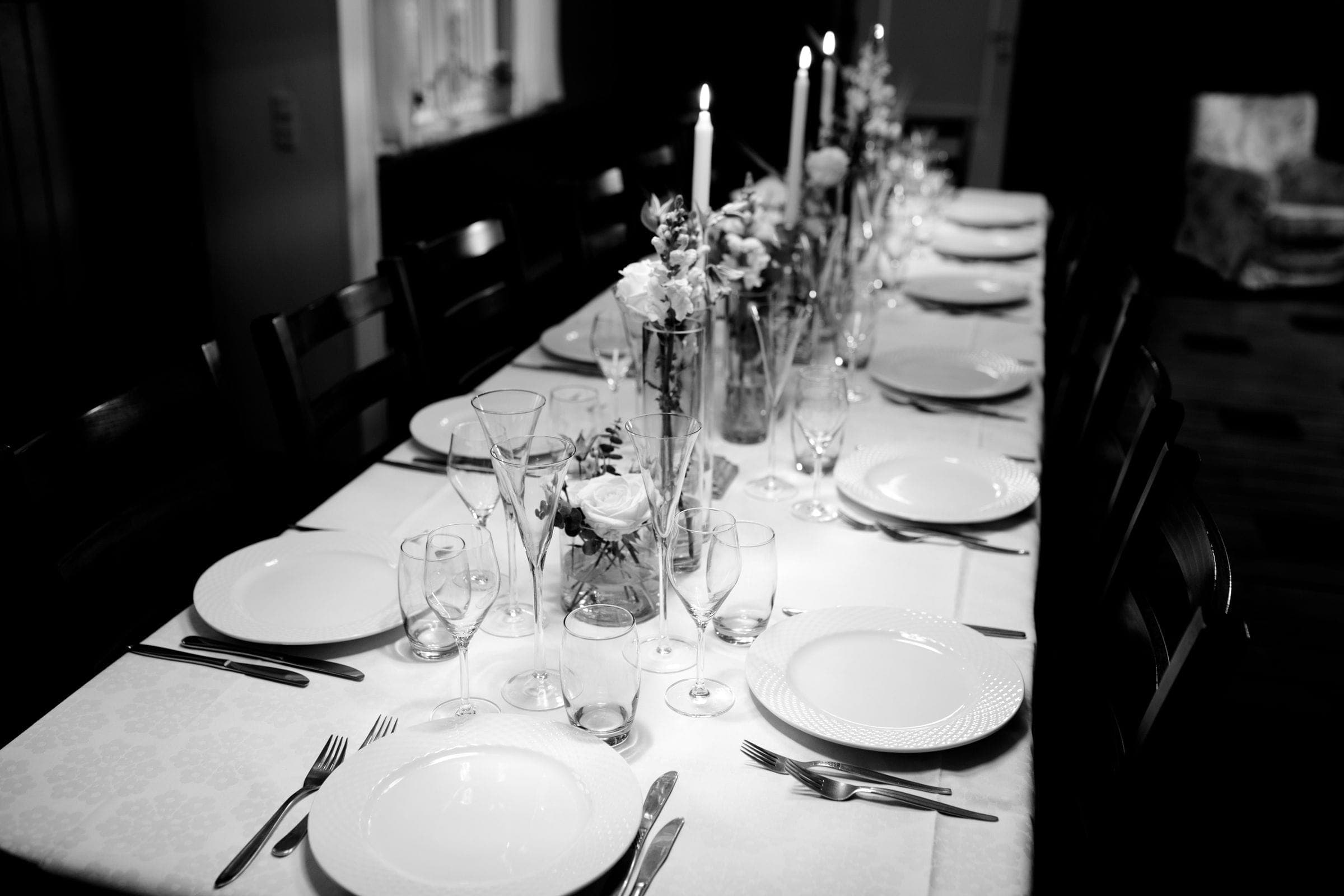 A long table set with candles and glassware, photographed in black and white